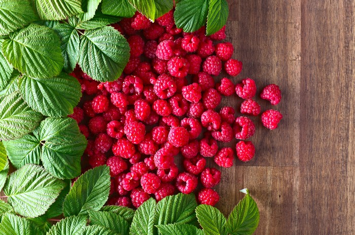 Raspberries and green leaves on a wooden background