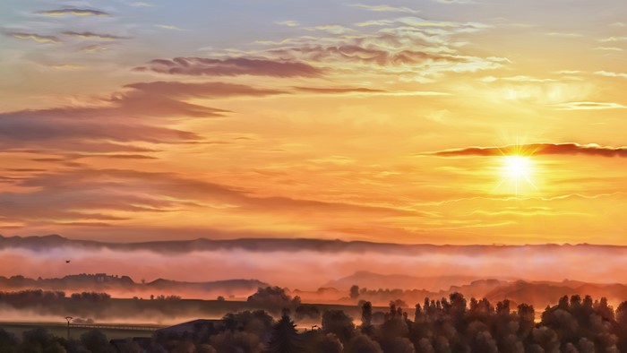 Sunrise over foggy landscape with sunbeams