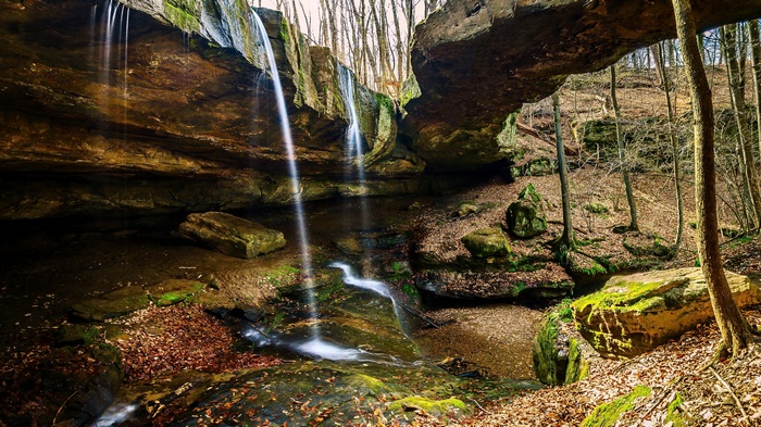 Waterfall flowing under a rock arch in a forest