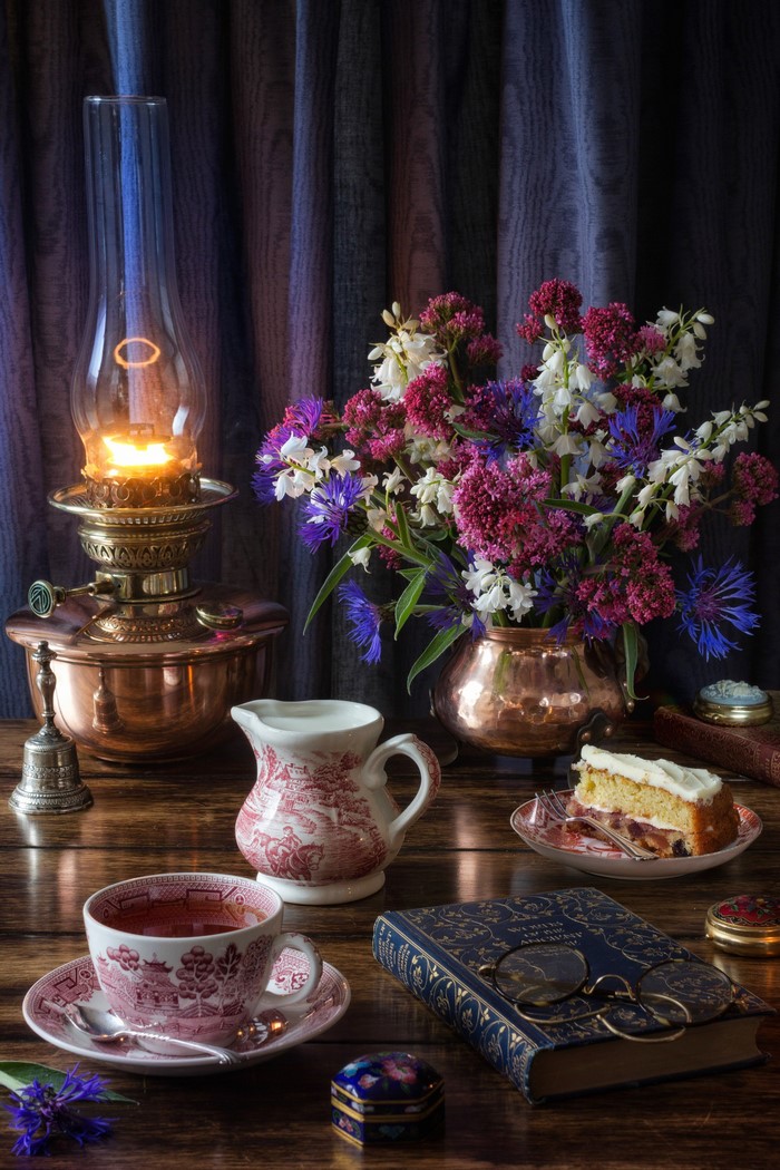Still life with kerosene lamp, flowers, tea, and cake