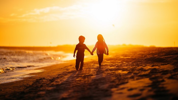 Children holding hands on a beach at sunset