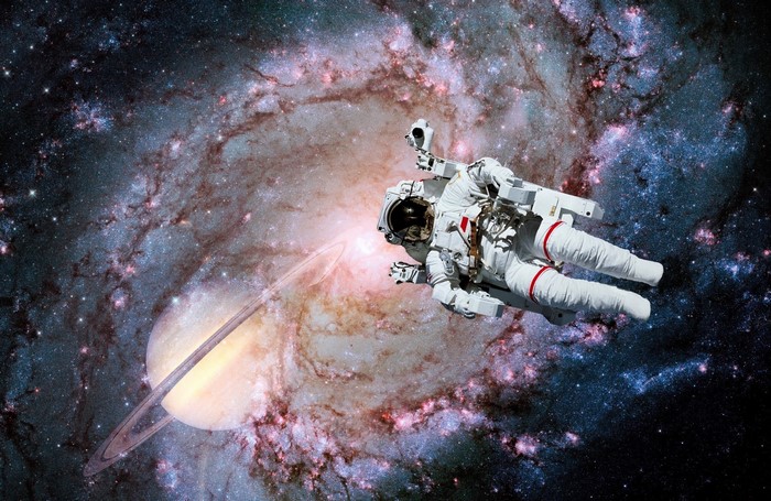 Astronaut floating near Saturn and galaxy