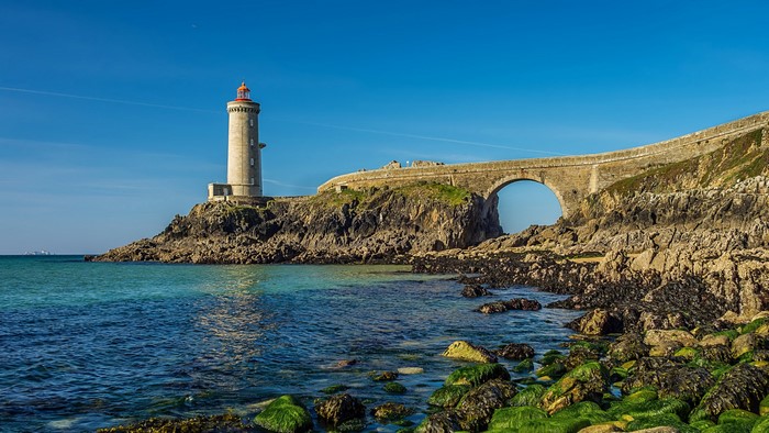 Lighthouse and stone bridge on a rocky coast in France
