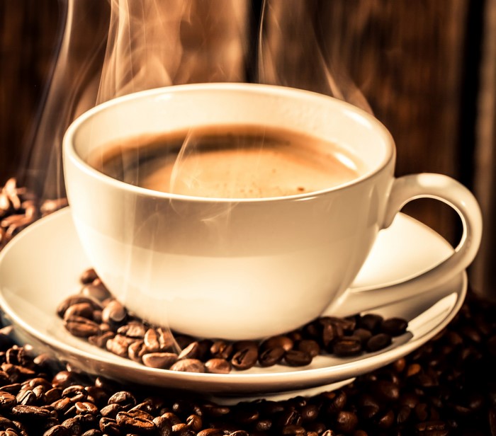 Hot coffee in a white cup with coffee beans