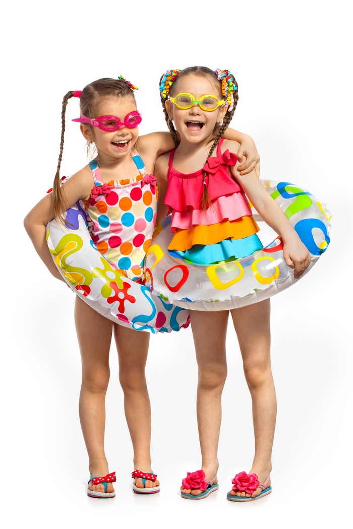 Two smiling girls in swimsuits and goggles with inflatable rings