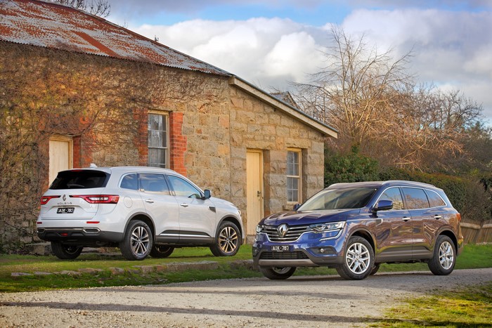 Two Renault Koleos cars parked near a stone building