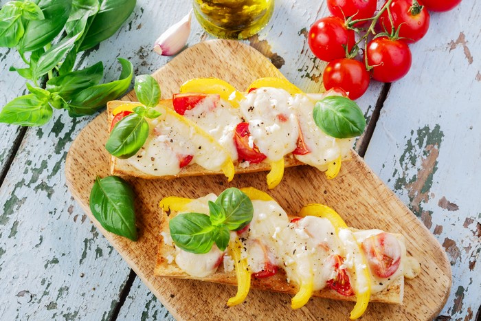 Open-faced sandwiches with melted cheese, tomatoes, and peppers