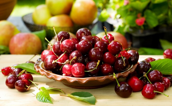 Cherries in a bowl with apples in the background