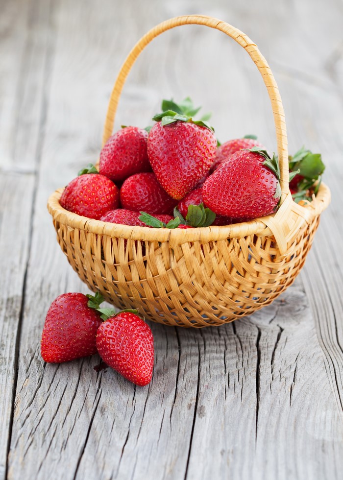 Strawberries in a wicker basket on wood planks