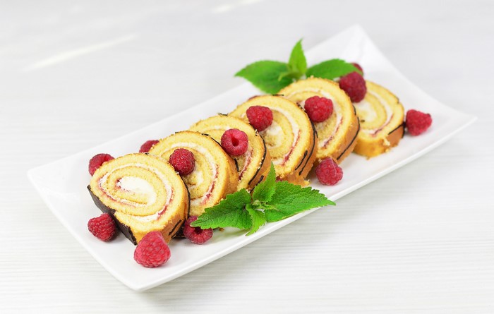 Swiss roll with raspberries and mint on a white plate