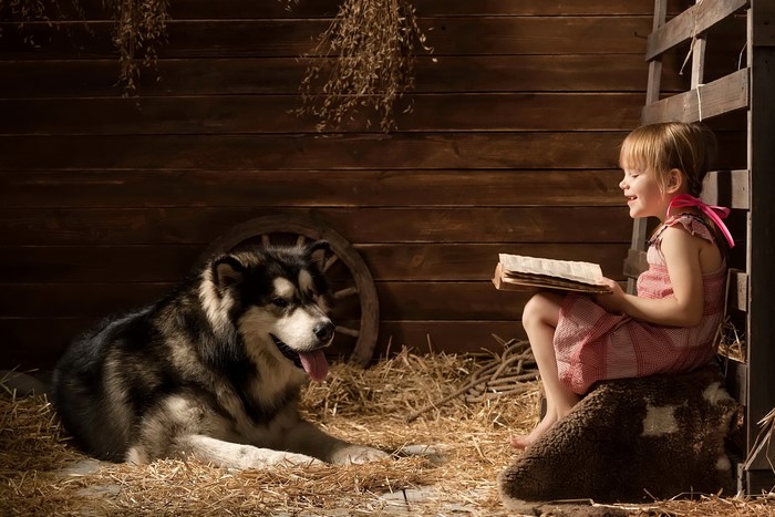 Girl reading a book to a dog in a barn