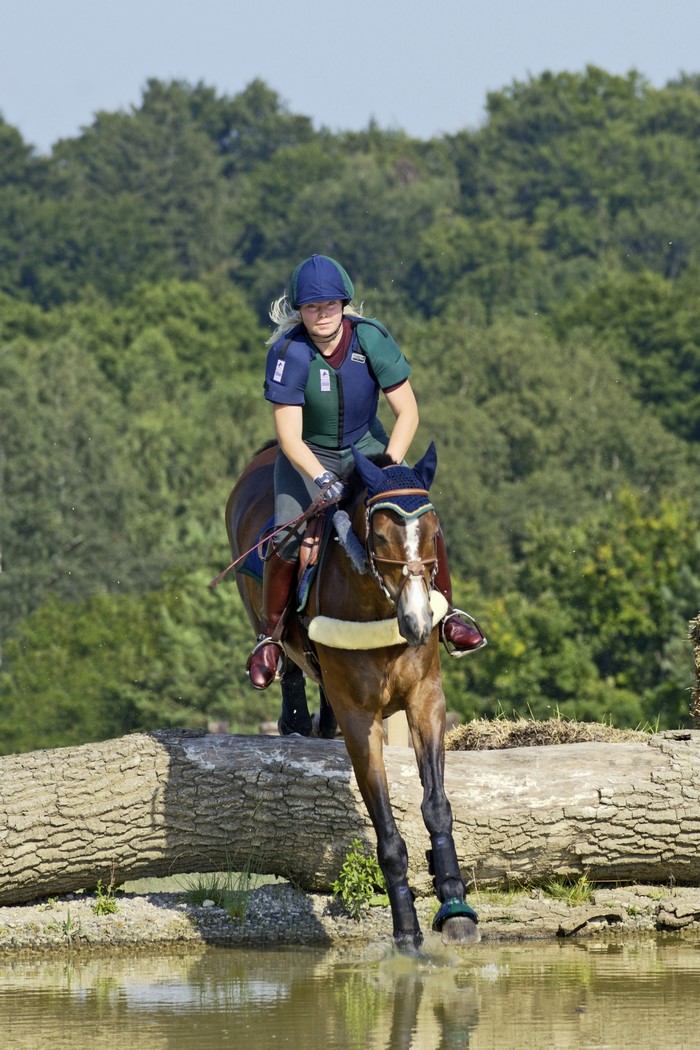 Woman riding a horse over a log jump