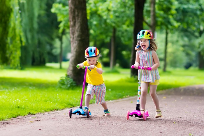 Two children riding scooters in a park