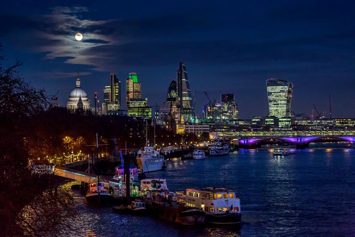 London skyline at night with moon over River Thames