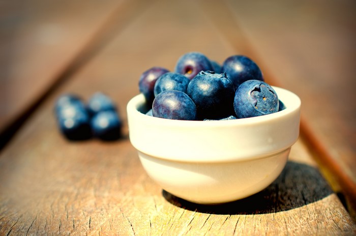 Blueberries in a white bowl on a wooden surface