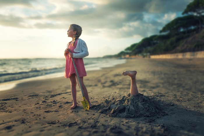 Girl with shovel on beach, buried leg