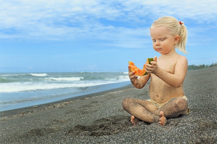 Little girl eating melon on a beach
