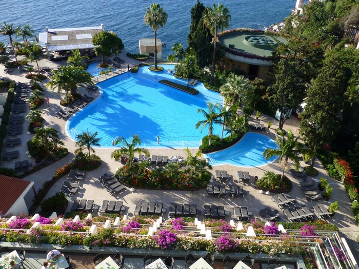 Resort pool area with sunloungers and palm trees by the sea in Madeira, Portugal
