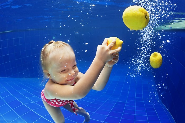 Little girl playing with lemons underwater in a pool