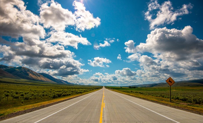 Open Road Through Green Fields Under Cloudy Sky