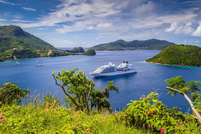 Cruise liner in a bay with green hills and sailboats