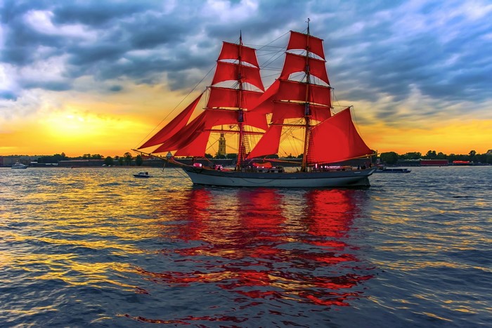 Tall ship with red sails on the water at sunset
