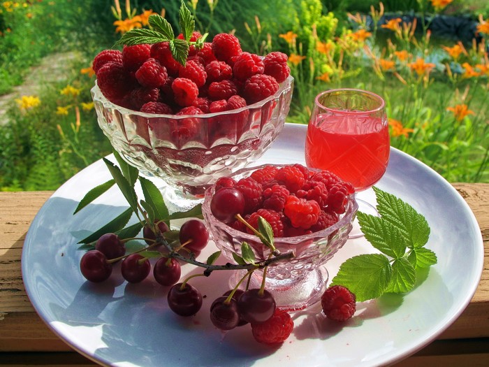 Raspberries and cherries with juice on a plate