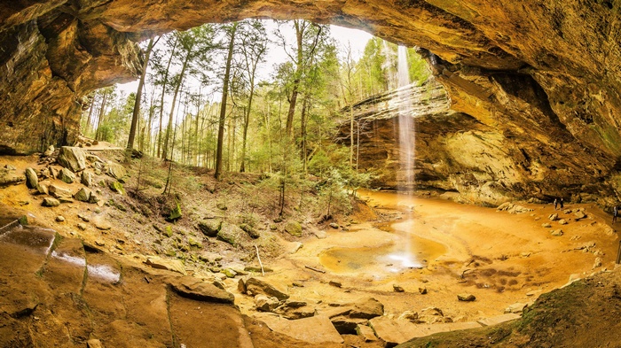 Waterfall cascading into a cave with trees and rocks
