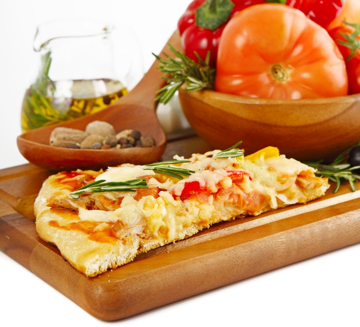 Slice of pizza with tomatoes and rosemary on cutting board