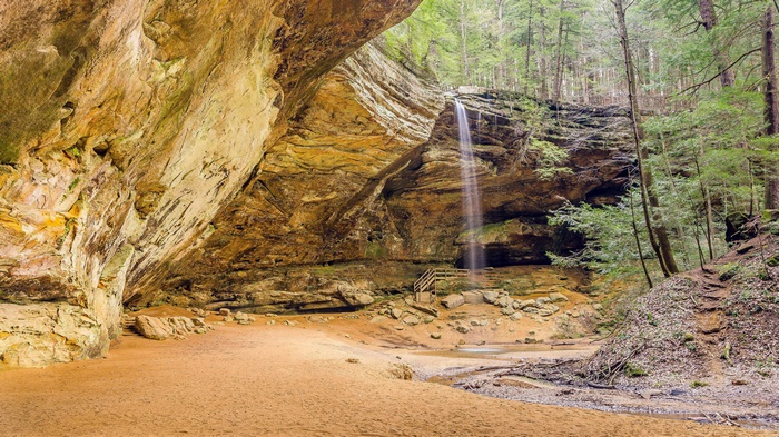 Waterfall cascading into a sandy cave with a forest backdrop