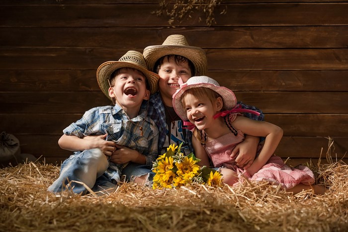 Three Children in Cowboy Hats with Sunflowers on Hay
