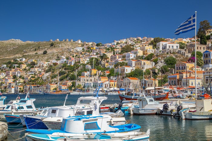 Boats docked in Symi, Greece with colorful houses on hillside
