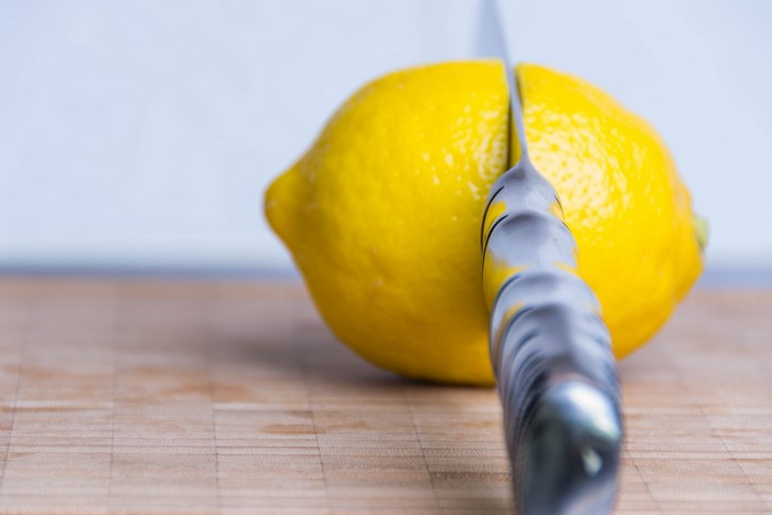 Lemon being cut by a knife on a cutting board
