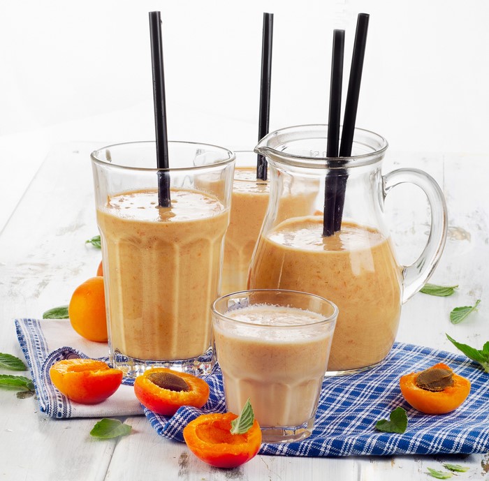 Apricot smoothie in glasses and pitcher with fresh apricots