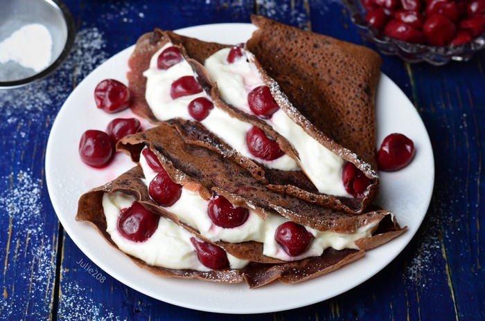 Chocolate crepes with cream and cherries on a plate