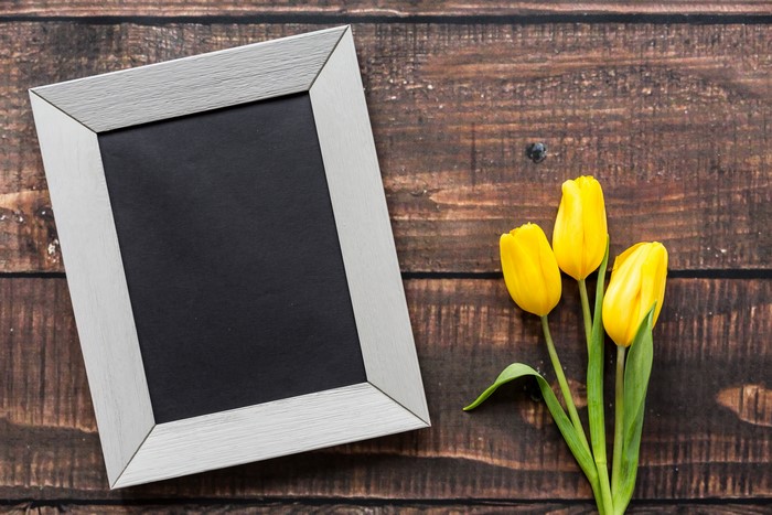 Silver picture frame with yellow tulips on wooden background