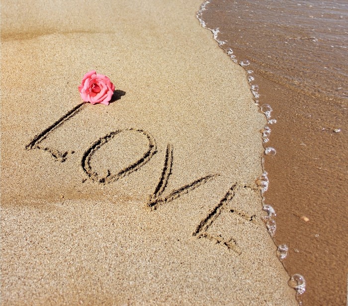 Love written in sand with a rose