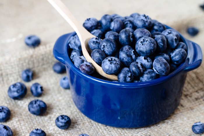Blueberries in a blue bowl with a wooden spoon