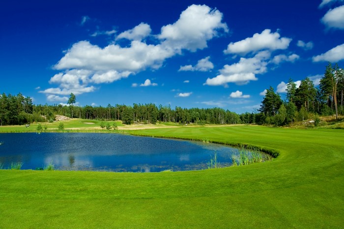 Golf course with pond and trees under blue sky