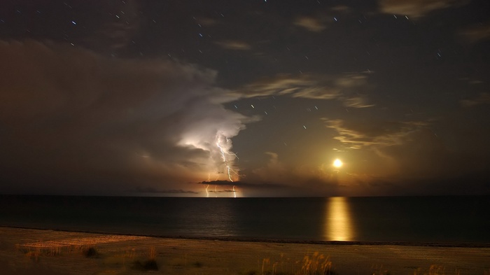 Lightning strikes over the ocean at night with moon