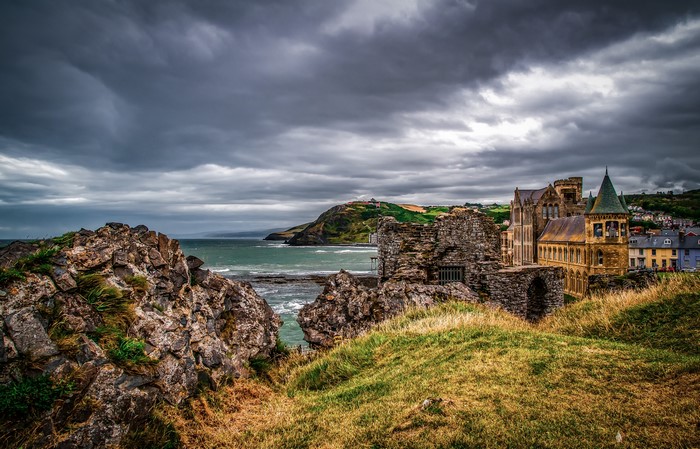 Ruins and buildings on a rocky coast under a cloudy sky
