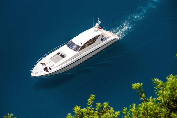 White yacht sailing on blue water with a dog on deck