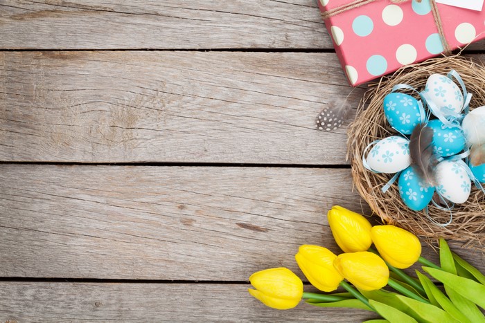 Easter eggs in a nest with tulips and gift box on wood