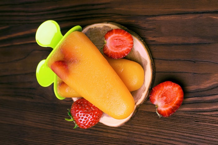 Orange popsicles with strawberries on a wooden table