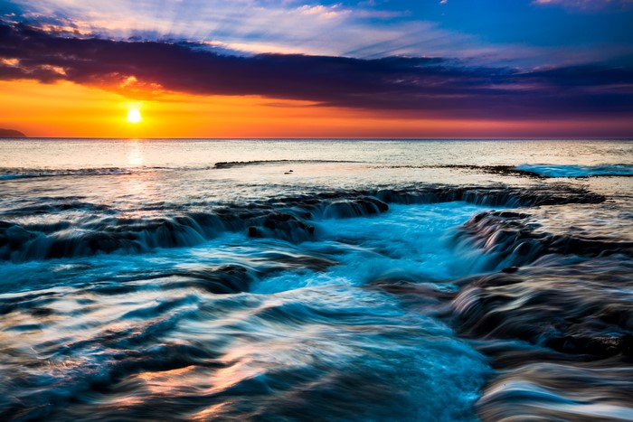 Sunset over the ocean with waves crashing on rocks