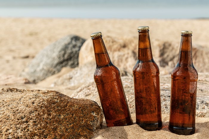 Three Beer Bottles on a Sandy Beach with Rocks