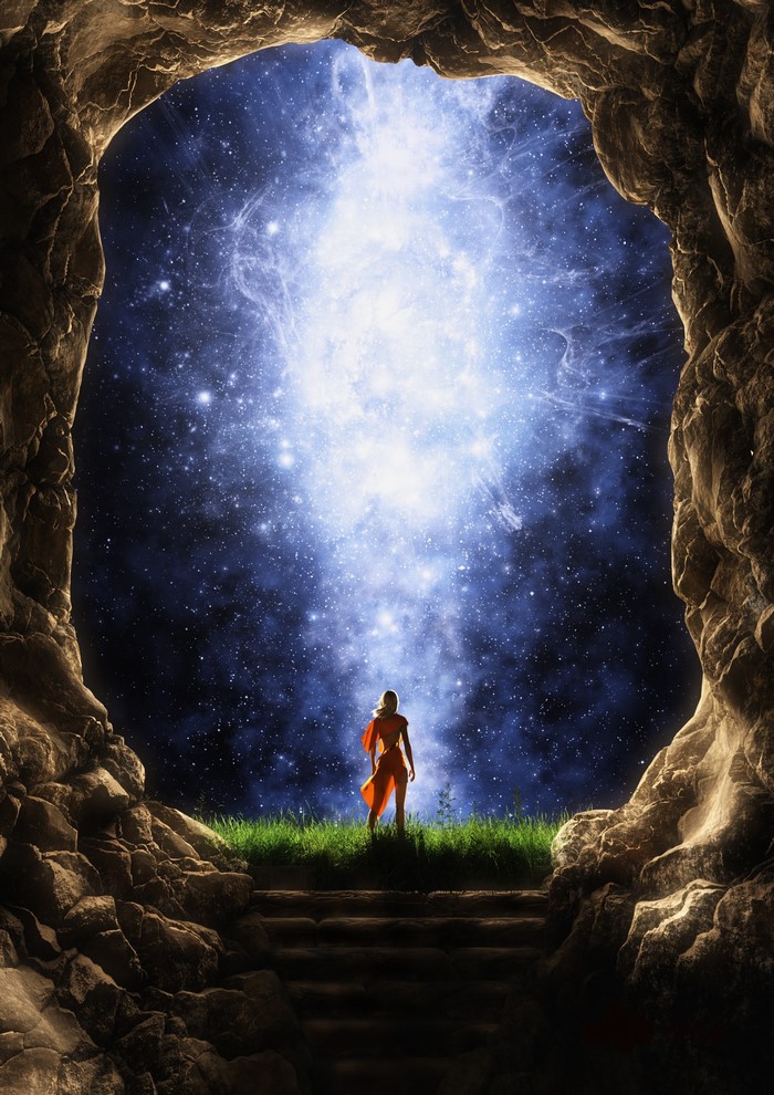 Person in orange robe looking at starry nebula from cave