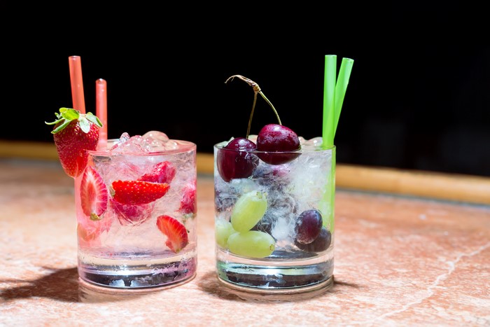 Two fruit-infused drinks with strawberries and cherries