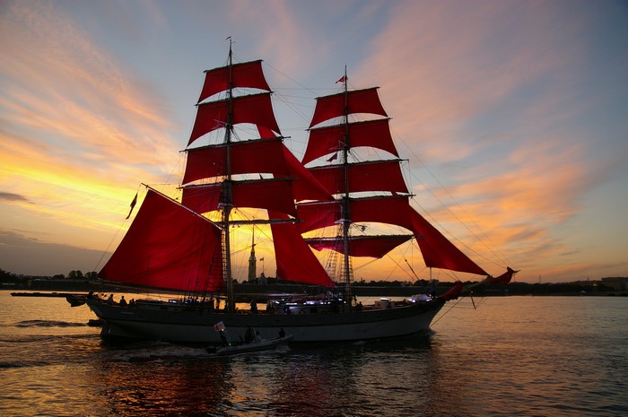 Sailing ship with red sails on a river at sunset