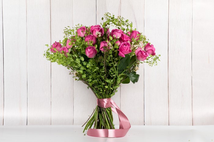 Bouquet of pink roses with green foliage tied with a pink ribbon